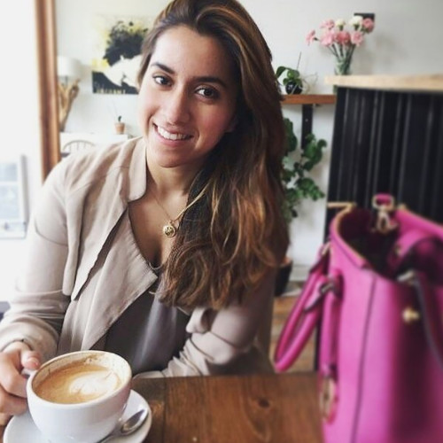 Woman in cream cardigan beside a bold pink bag holding a cup of coffee.